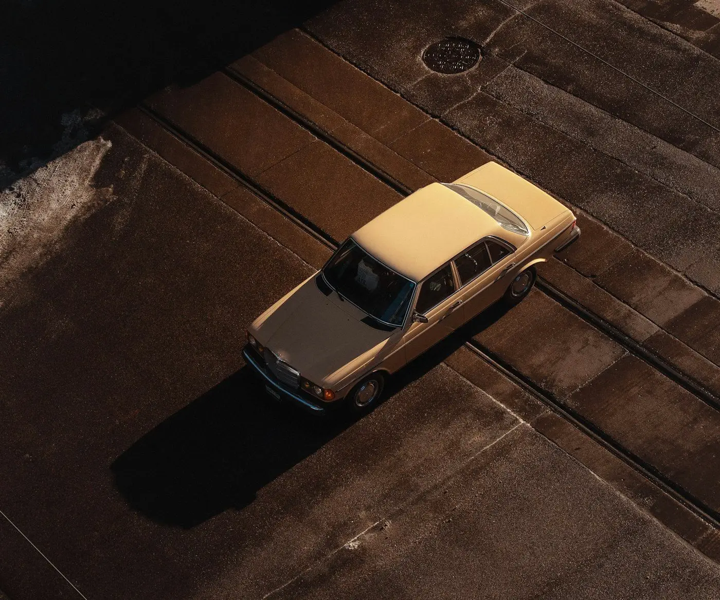 An older sedan crossing railroad tracks on a wet winter street, seen from above, in black and white