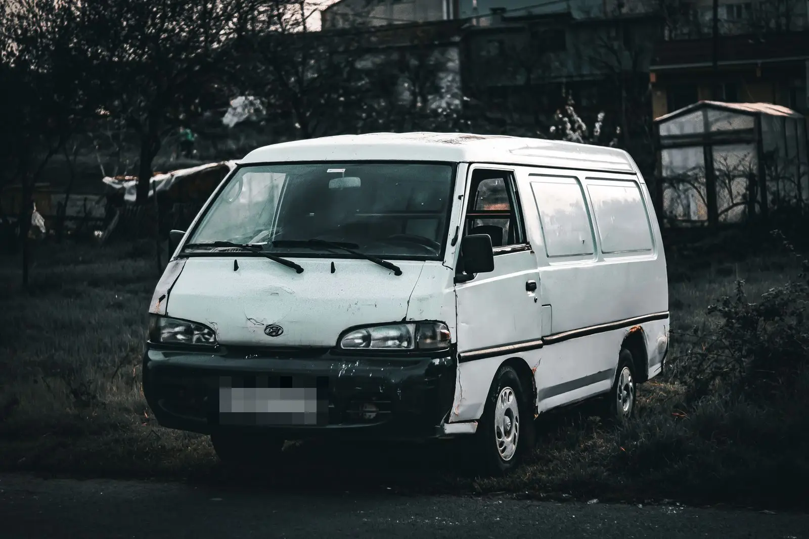 A worn white cargo van parked on grass at dusk, in black and white